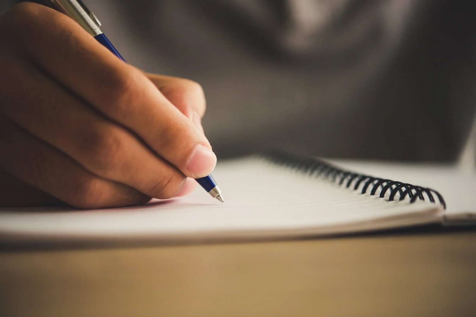 Main qui écrit au stylo dans un carnet, gros plan. Chapitre services, Guides, Cahier, Glossaire, Tarifs.